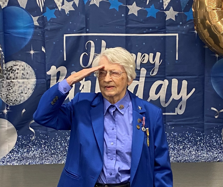 Photo of General Vaught saluting with happy birthday banner in background
